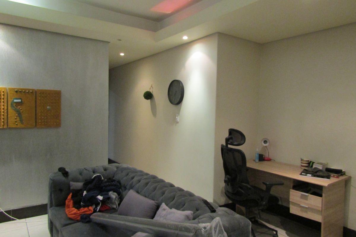 A living area featuring recessed ceiling lighting and tiled flooring, currently utilized as a multi-functional space with a desk and seating.