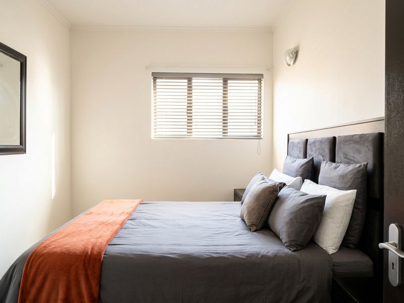 A well-maintained bedroom featuring neutral walls, a window with venetian blinds, and a wall-mounted light fixture.