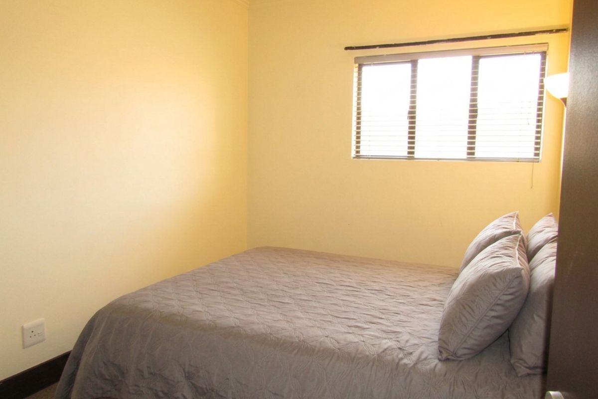 A simple bedroom featuring neutral walls, a window with fitted blinds, and standard electrical fixtures.