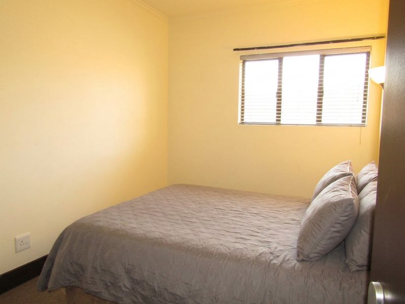 A simple bedroom featuring neutral walls, a window with fitted blinds, and standard electrical fixtures.
