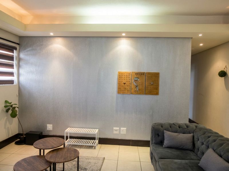 A well-lit living room featuring neutral tiled flooring, recessed ceiling lighting, and a textured feature wall with integrated electrical points.
