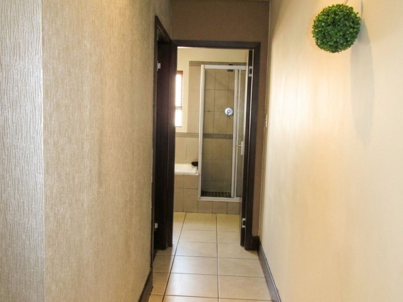 A neutral hallway with tiled flooring and textured wall finishes, leading directly into a bathroom with a shower enclosure.