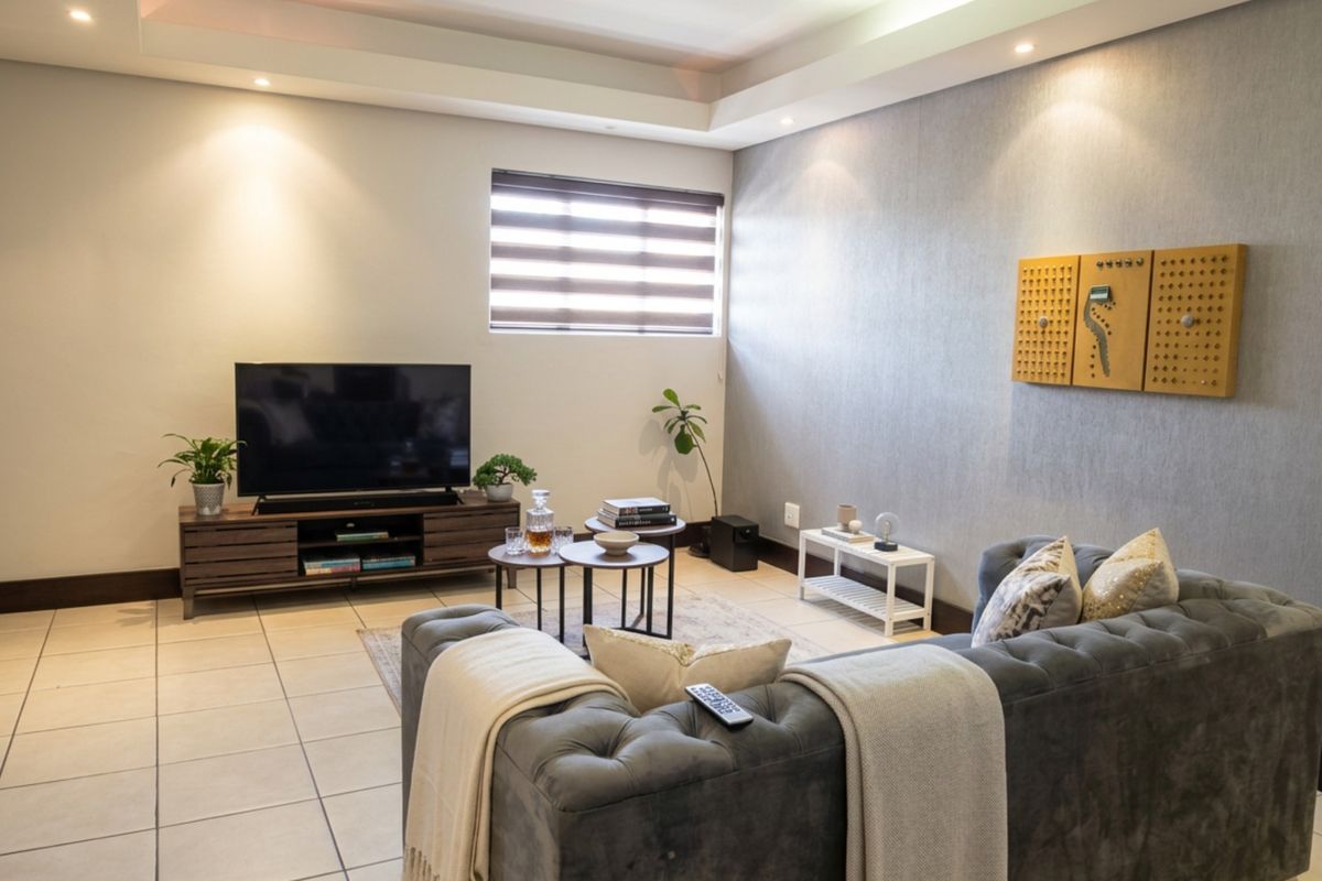 A well-lit living room featuring tiled flooring, a modern drop ceiling with recessed lighting, and neutral wall finishes with a textured accent wall.
