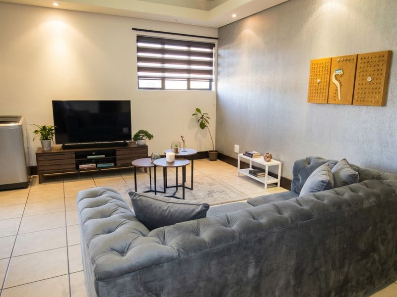 A well-lit living room featuring neutral tiled flooring, recessed ceiling lighting, and modern roller blinds, creating a comfortable and functional living space.