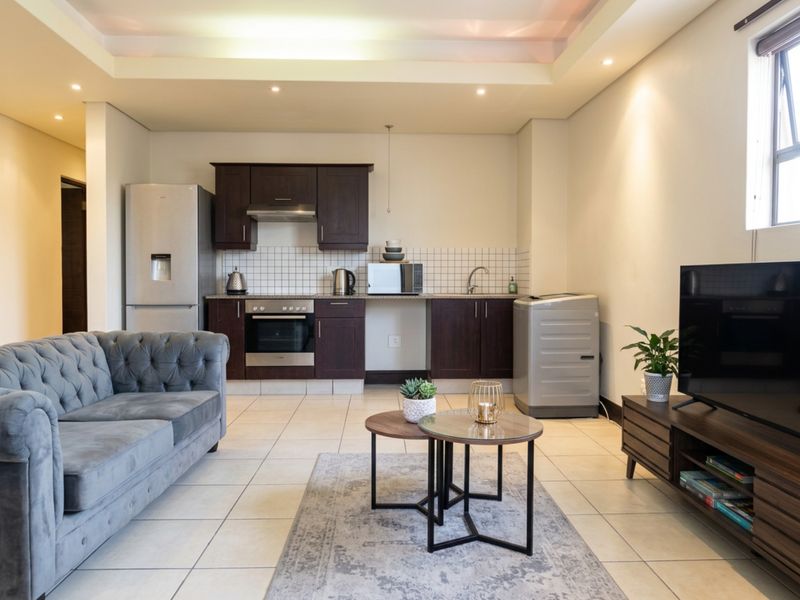 Modern open-plan living area featuring a well-appointed kitchen with dark wood cabinetry, tiled backsplash, and integrated appliances, flowing into a comfortable lounge space.