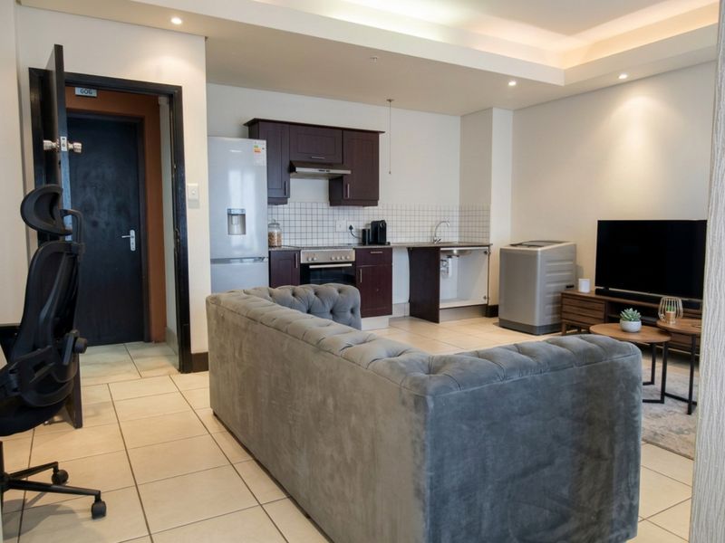 Open-plan living area featuring a compact kitchen with dark cabinetry, tiled flooring, and recessed lighting, seamlessly integrated with the lounge space.