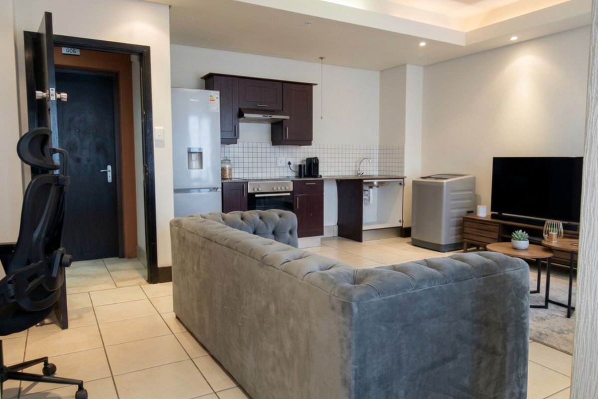 Open-plan living area featuring a compact kitchen with dark cabinetry, tiled flooring, and recessed lighting, seamlessly integrated with the lounge space.