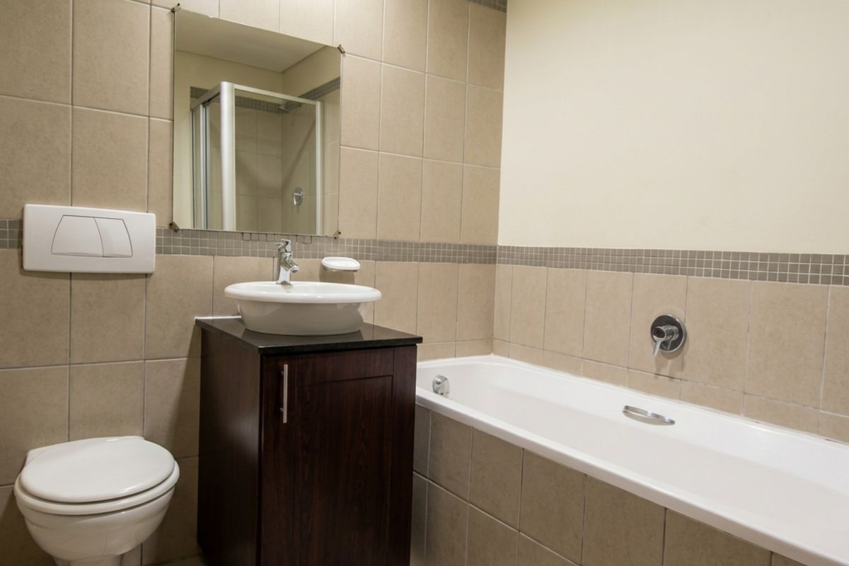 A clean, functional bathroom featuring a vessel sink vanity, wall-mounted toilet, and a built-in bathtub with neutral wall tiling.