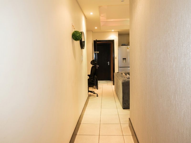 A well-lit hallway featuring neutral tiled flooring and recessed ceiling lights, providing a clean transition between the living area and other rooms.