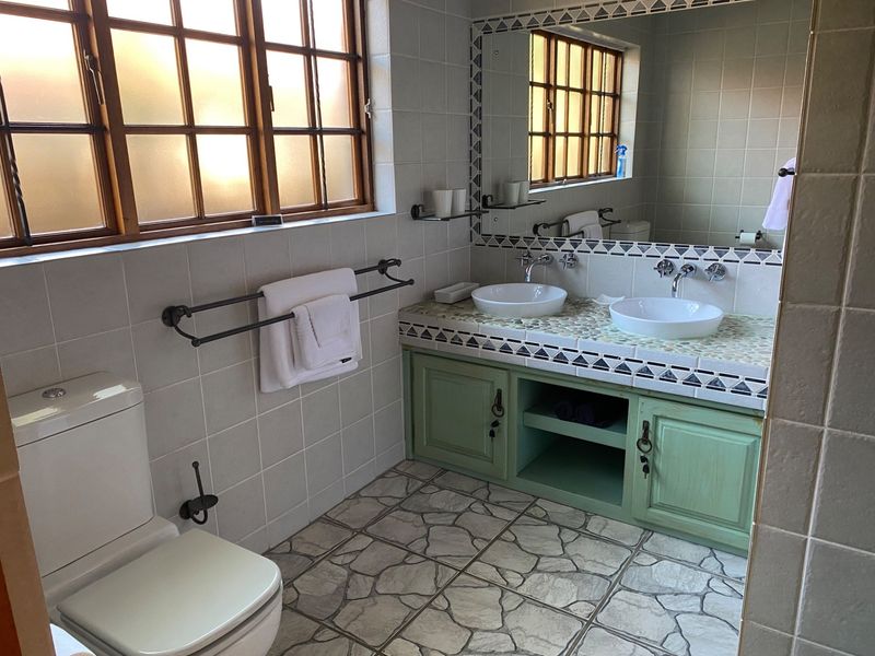 A bathroom featuring a double vanity with vessel sinks, tiled countertops, built-in green cabinetry, and large wall mirror with timber-framed windows.