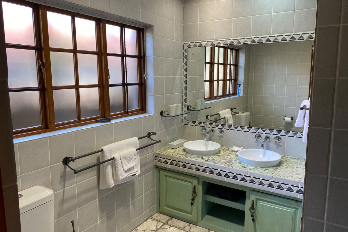 A functional bathroom featuring a double vanity with vessel sinks, tiled surfaces, and a timber-framed window, offering a classic, lived-in aesthetic.