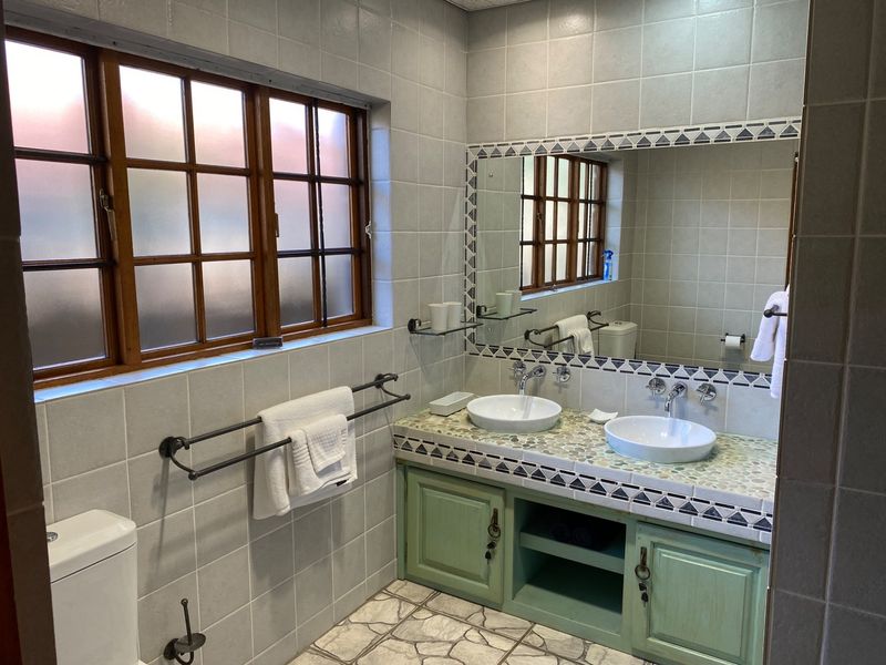 A functional bathroom featuring a double vanity with vessel sinks, tiled surfaces, and a timber-framed window, offering a classic, lived-in aesthetic.