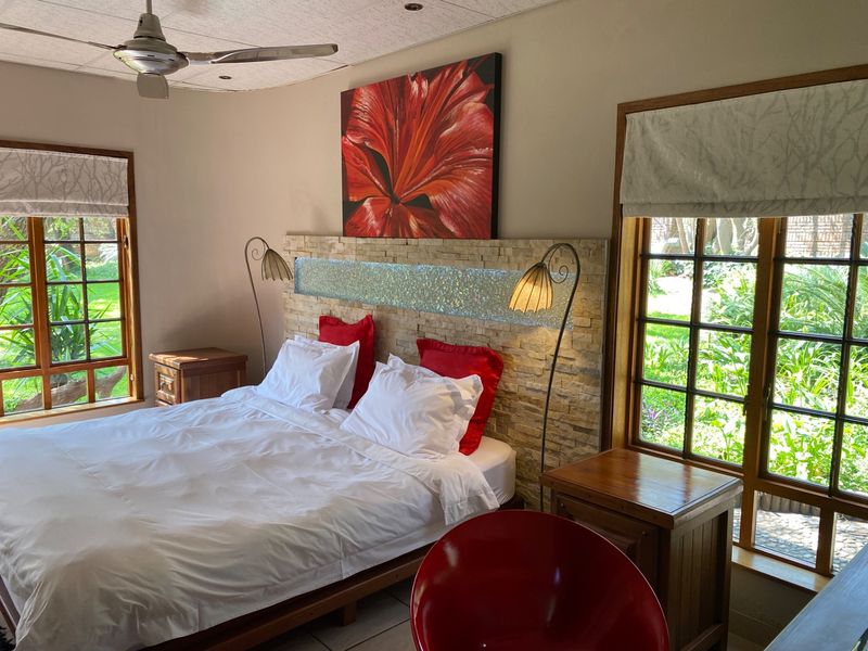 A well-lit bedroom featuring a stone veneer headboard wall, timber-framed windows overlooking the garden, and a ceiling fan.