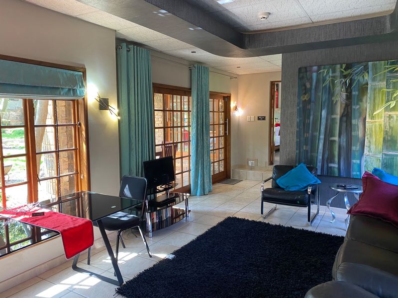 A well-lit living area featuring tiled floors, wooden framed glass doors providing garden access, and a modern drop ceiling design with integrated lighting.
