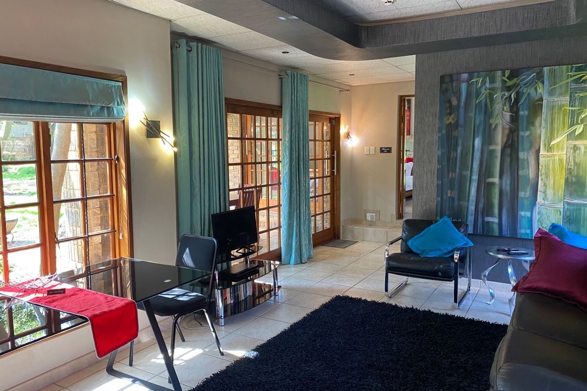 A well-lit living area featuring tiled floors, wooden framed glass doors providing garden access, and a modern drop ceiling design with integrated lighting.