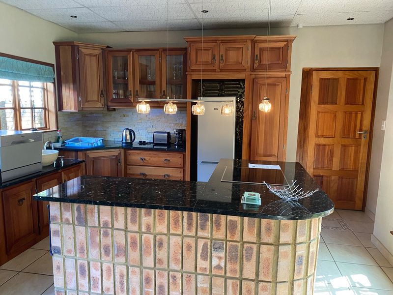 A kitchen featuring wooden cabinetry, granite countertops, a brick breakfast bar, and built-in hob, offering a traditional aesthetic with functional layout.