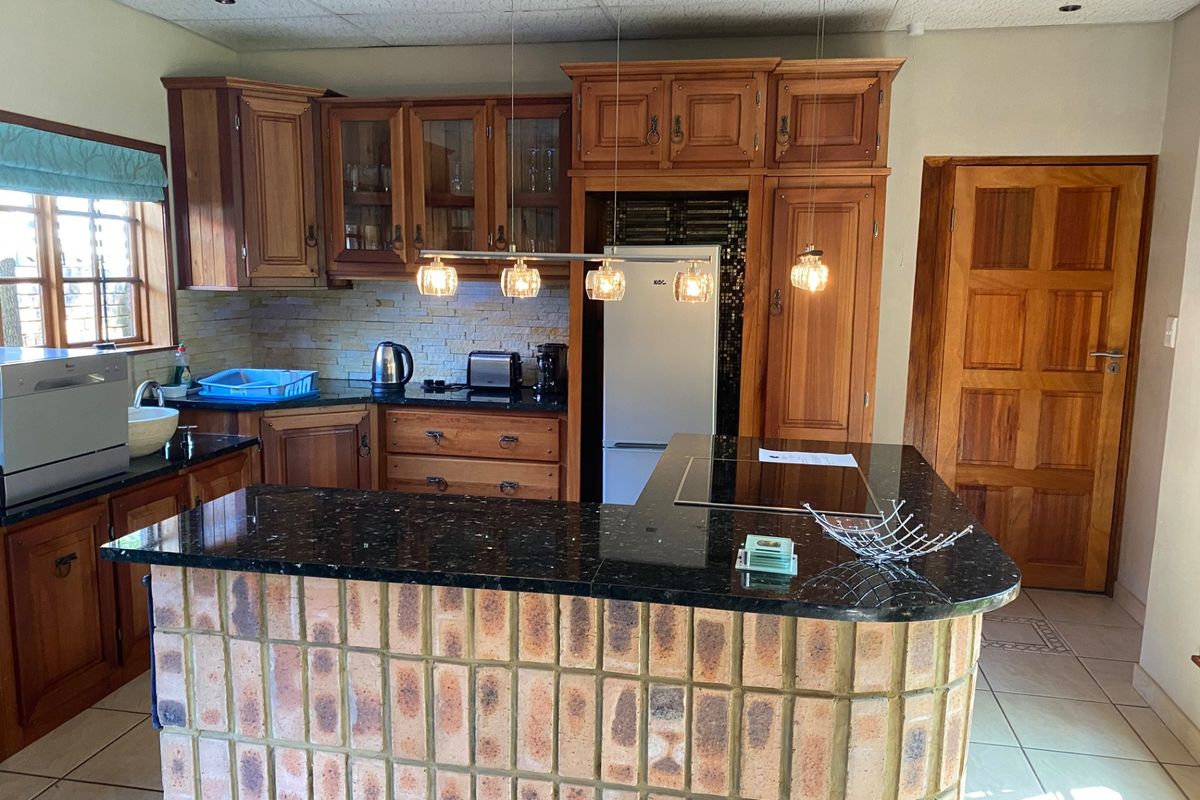 A kitchen featuring wooden cabinetry, granite countertops, a brick breakfast bar, and built-in hob, offering a traditional aesthetic with functional layout.