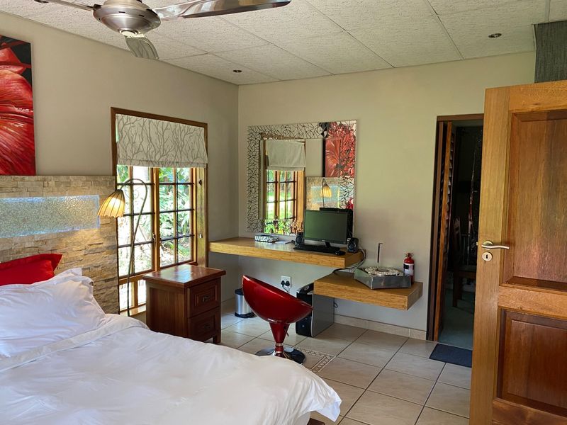 A well-maintained bedroom featuring a stone accent wall, built-in desk workspace, tiled flooring, and a ceiling fan, offering a functional and comfortable living space.