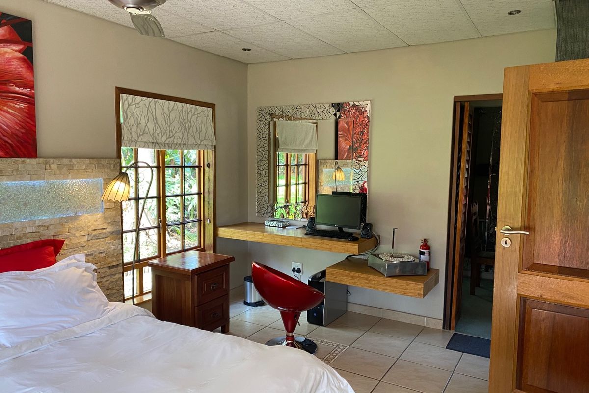 A well-maintained bedroom featuring a stone accent wall, built-in desk workspace, tiled flooring, and a ceiling fan, offering a functional and comfortable living space.