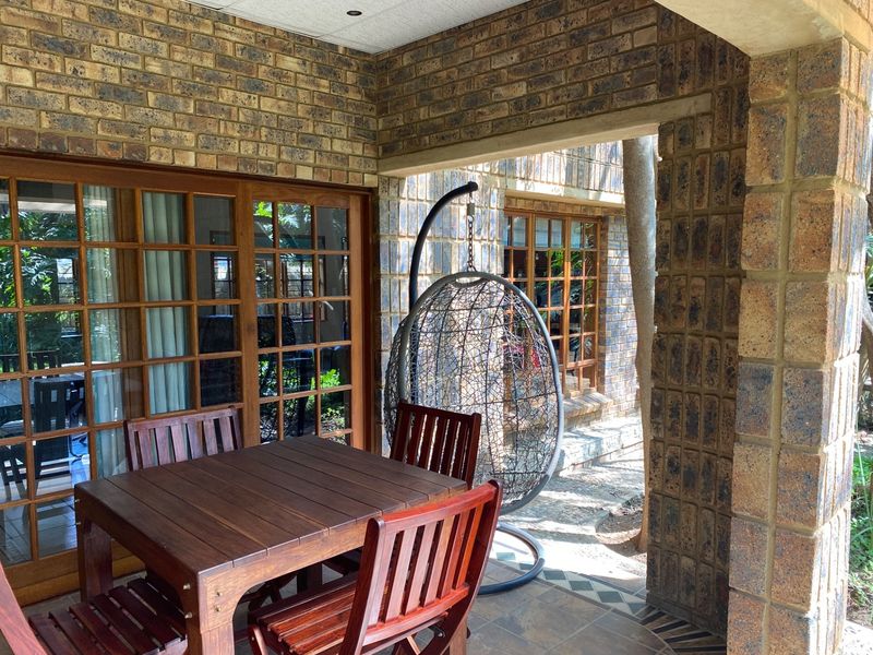 A covered patio area featuring exposed brick walls, tiled flooring, and wooden framed glass sliding doors providing access to the interior.