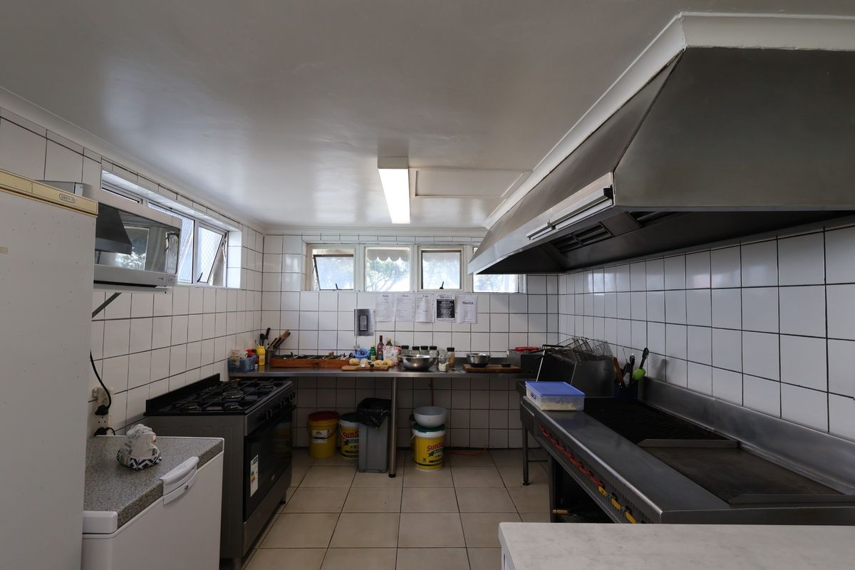 A functional commercial kitchen featuring stainless steel prep counters, a gas stove, a commercial grill, and a large extractor hood with tiled finishes.