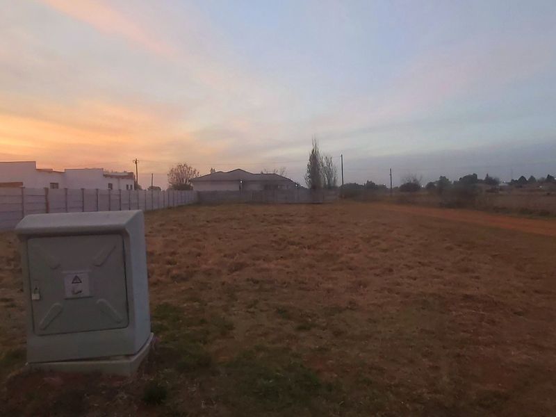 A vacant residential plot featuring a precast concrete boundary wall and an installed electrical utility box at sunset.