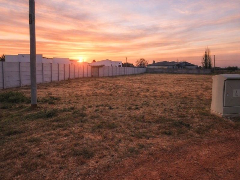 A vacant residential plot featuring a precast concrete boundary wall, utility pole, and electrical connection point at sunset.