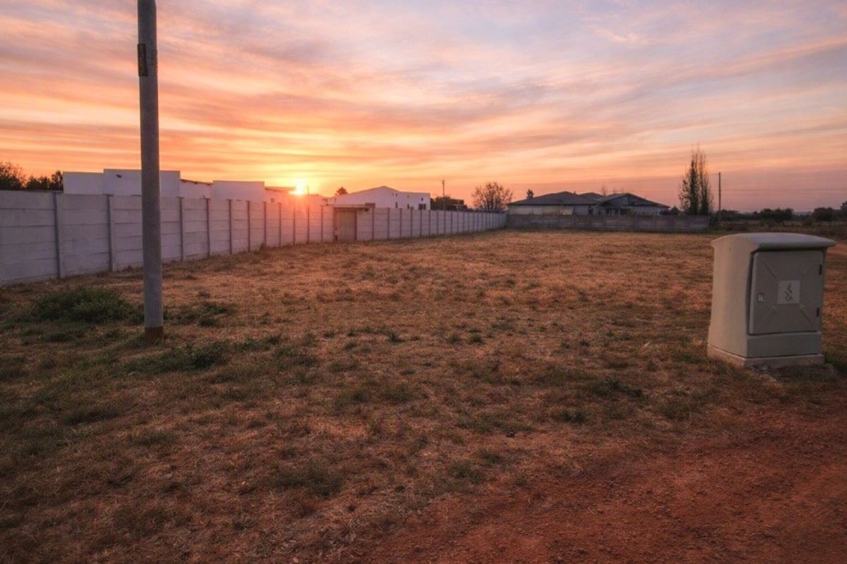 A vacant residential plot featuring a precast concrete boundary wall, utility pole, and electrical connection point at sunset.