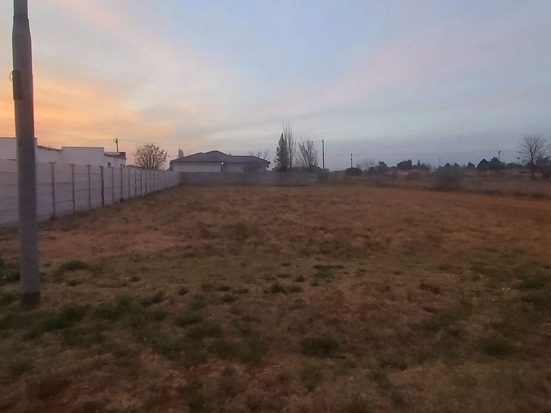 A vacant residential plot featuring a precast concrete boundary wall, utility pole, and electrical connection box at sunset.