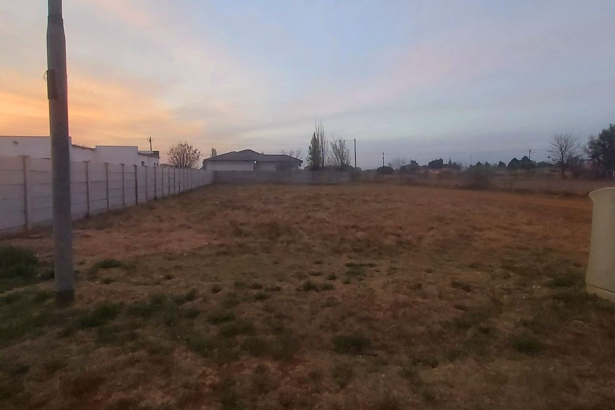 A vacant residential plot featuring a precast concrete boundary wall, utility pole, and electrical connection box at sunset.