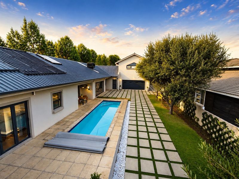Aerial view of a well-maintained rear exterior featuring a swimming pool, paved patio area, landscaped garden, and modern metal roof with solar panels.