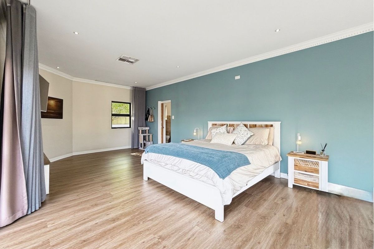 Spacious bedroom featuring modern laminate flooring, recessed downlighting, and a feature wall, offering a bright and comfortable living space.