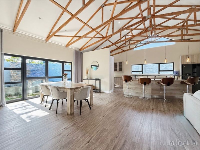 Spacious open-plan living and dining area featuring high vaulted ceilings with exposed timber trusses, modern kitchen island, and large sliding doors leading outdoors.