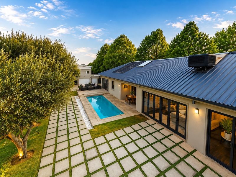 Rear exterior view featuring a modern swimming pool, paved patio area, and bi-fold doors leading into the home, set against a landscaped garden.