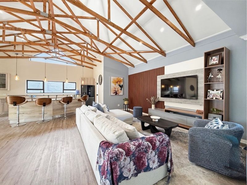 Spacious open-plan living area featuring a striking vaulted ceiling with exposed timber trusses, a modern kitchen island, and a contemporary slatted feature wall.