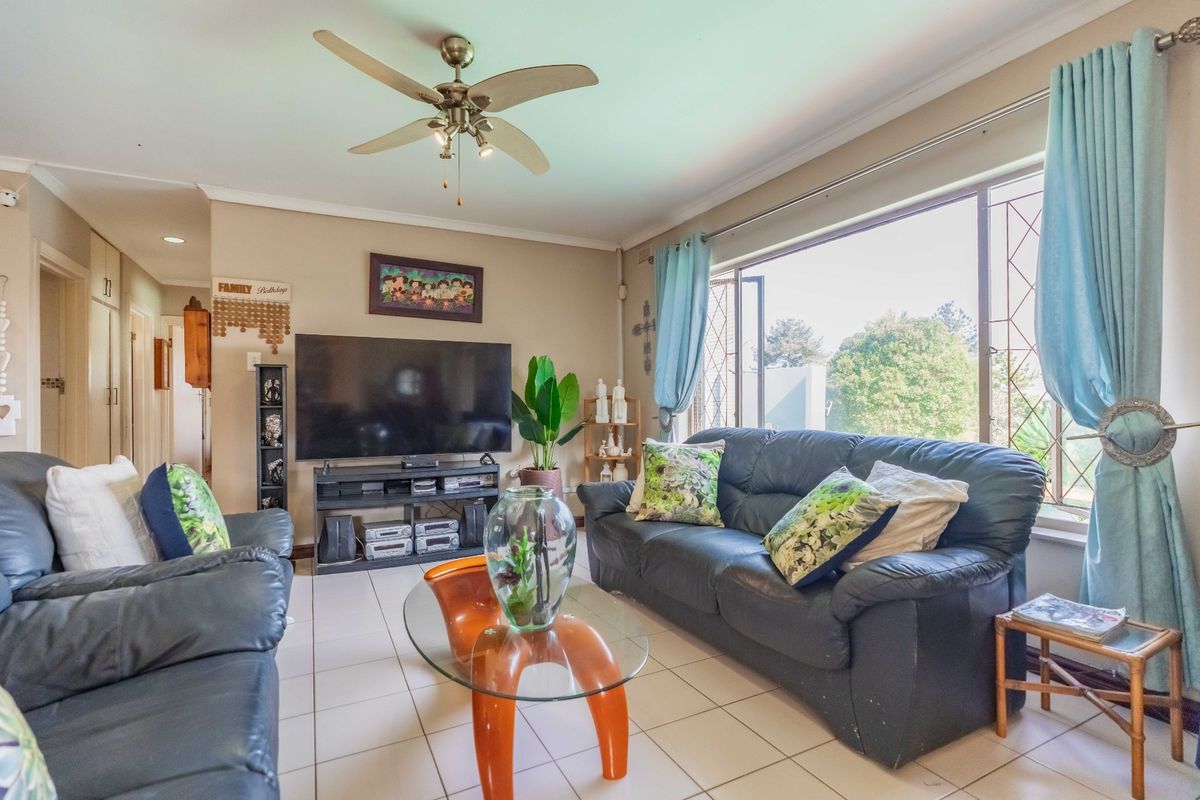A comfortable living room featuring tiled flooring, a ceiling fan, and a large window that provides natural light.