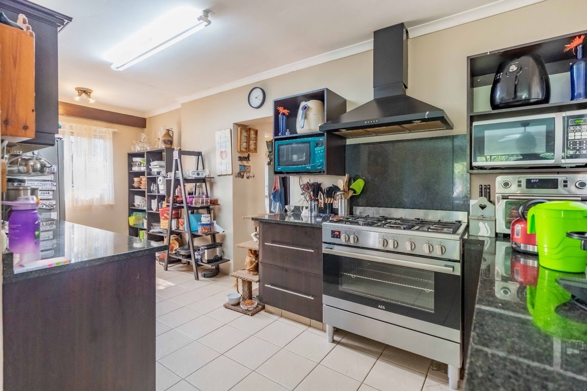 A functional kitchen featuring dark cabinetry, granite countertops, a gas stove with an extractor fan, and tiled flooring.
