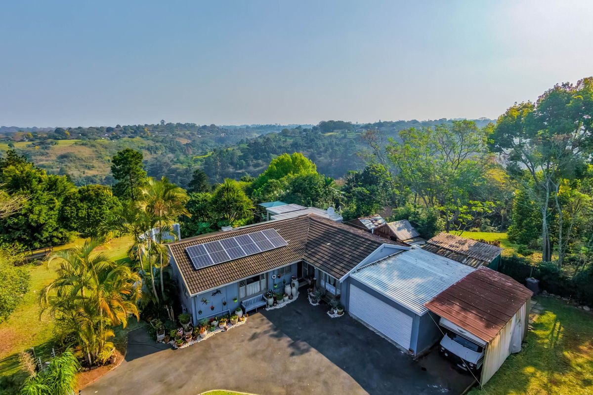 Aerial view of a residential property featuring a tiled roof with solar panels, a double garage, and an attached carport set in a landscaped garden.