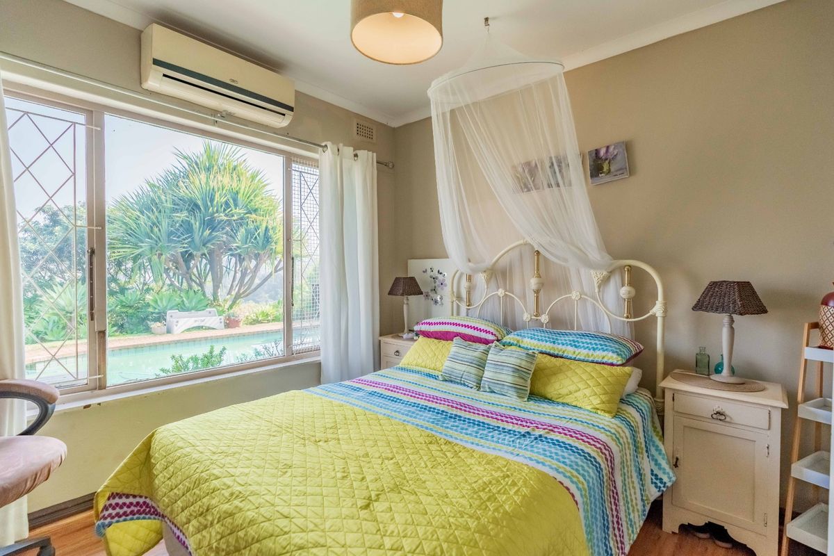 A bedroom featuring laminate flooring, a wall-mounted air conditioning unit, and a large window with security bars overlooking the pool area.