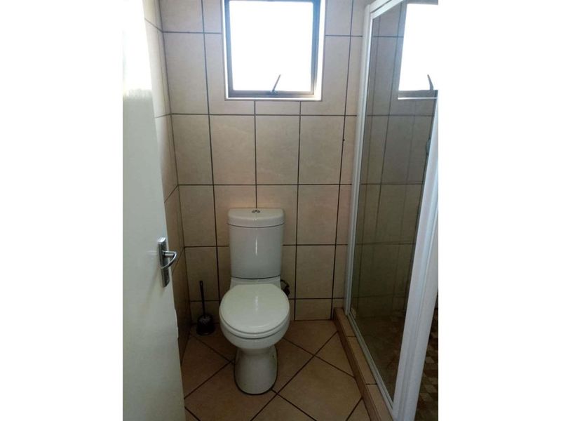 A compact bathroom featuring a standard toilet, a shower enclosure with a glass door, and neutral wall and floor tiling.