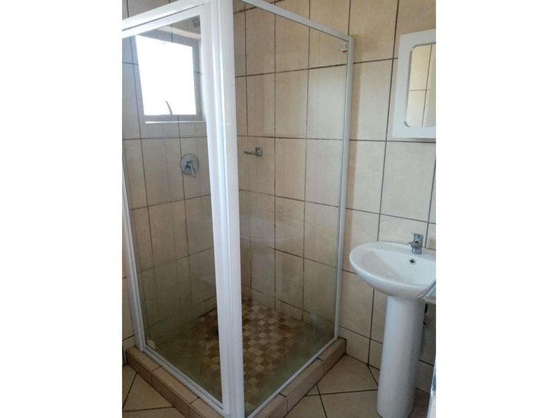 A functional bathroom featuring a corner shower enclosure, pedestal basin, and neutral wall and floor tiling.