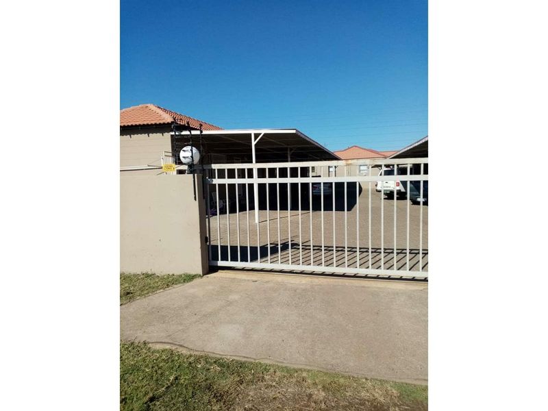 Front view of the property featuring a secure metal sliding gate, concrete driveway, and a covered carport area.