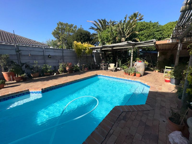 Outdoor pool area featuring a swimming pool, brick paved surround, and a timber pergola, set within a private garden with boundary walling.