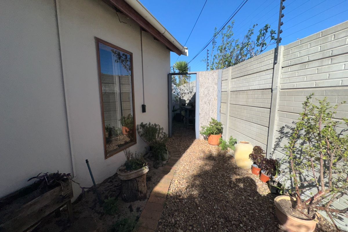 A side passage featuring a gravel pathway, precast concrete boundary wall with electric fencing, and a timber-framed window along the exterior wall.