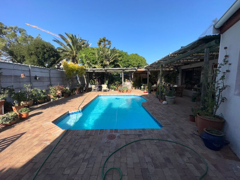 Outdoor pool area featuring a swimming pool surrounded by brick paving and a timber pergola, enclosed by a precast concrete boundary wall.