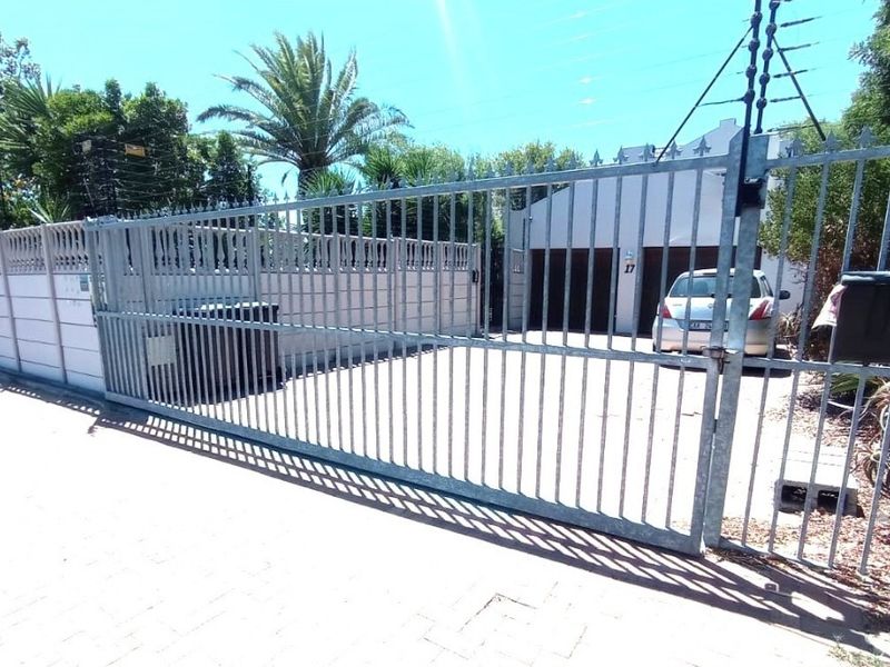 Front view of the property featuring a galvanized steel sliding gate, paved driveway, double garage, and secure boundary wall with electric fencing.