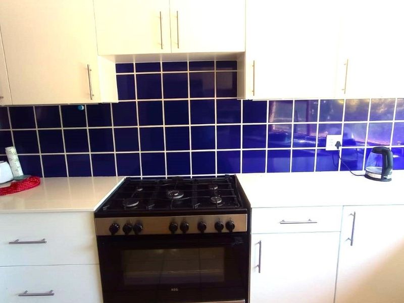 A functional kitchen featuring white cabinetry, a contrasting blue tiled backsplash, and a built-in gas stove with oven.