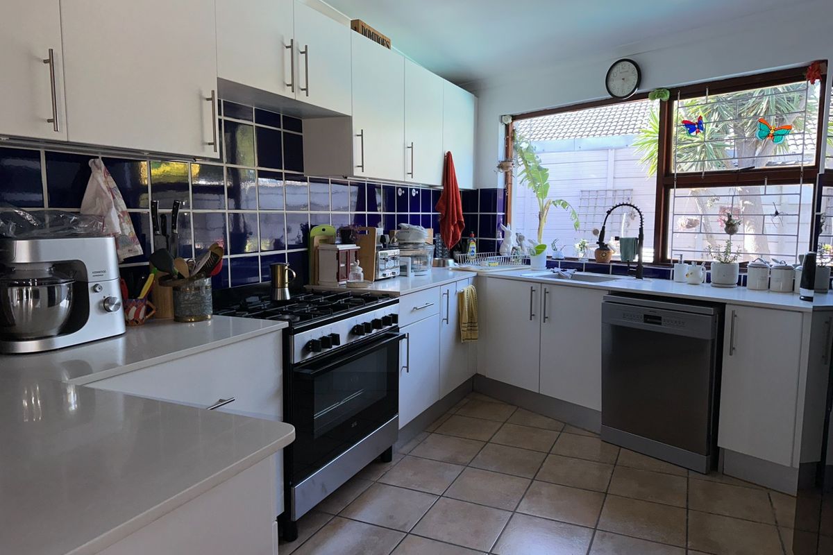 Functional kitchen featuring white cabinetry, dark blue tiled splashback, gas stove, and tiled flooring with ample natural light from the window.