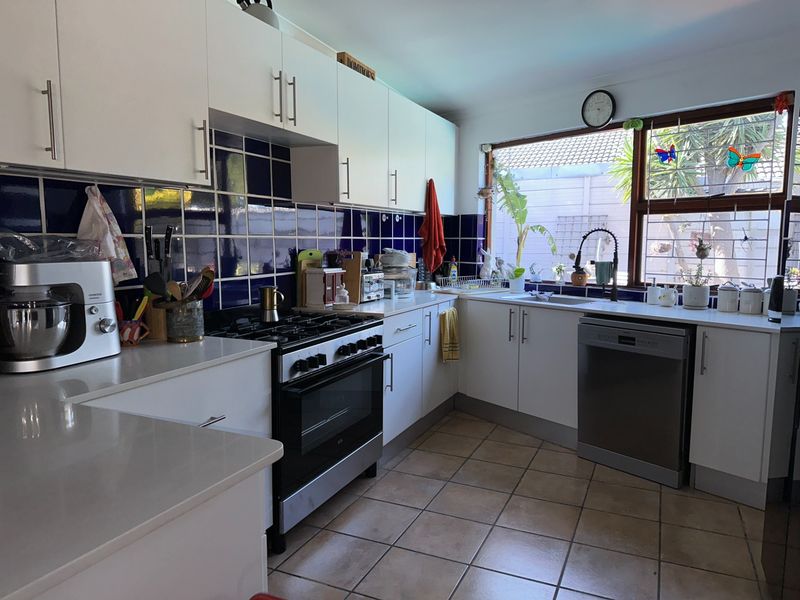 Functional kitchen featuring white cabinetry, dark blue tiled splashback, gas stove, and tiled flooring with ample natural light from the window.