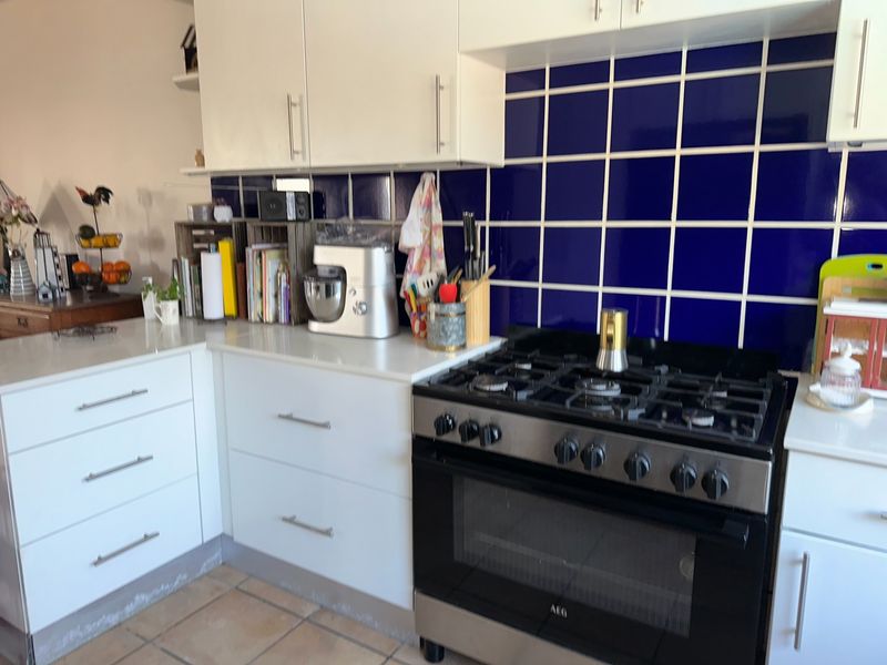 A functional kitchen featuring white cabinetry, stone countertops, a bold blue tiled backsplash, and a stainless steel gas range with oven.